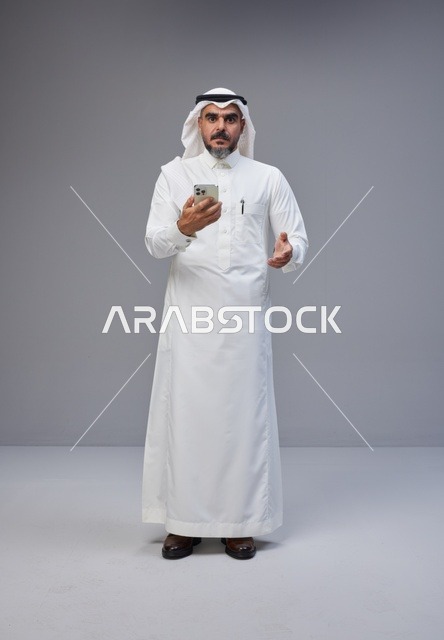 رجل سعودي بالزي التقليدي يستخدم الهاتف الذكي