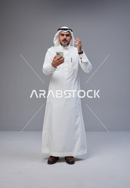 رجل سعودي بالزي التقليدي يستخدم الهاتف الذكي