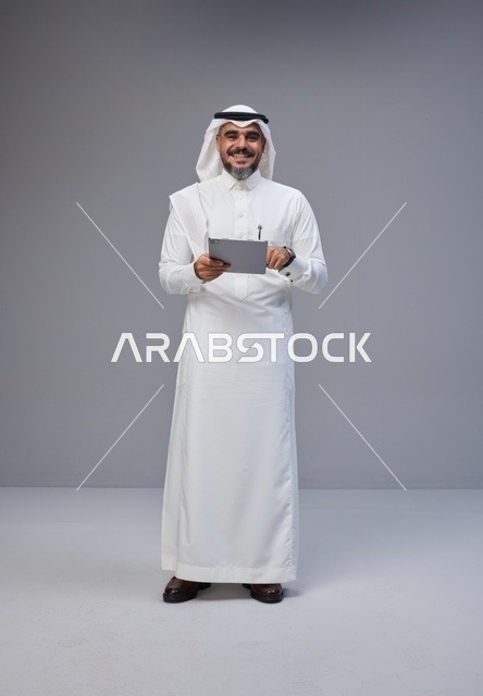 رجل سعودي بالزي التقليدي يستخدم جهازاً لوحياً