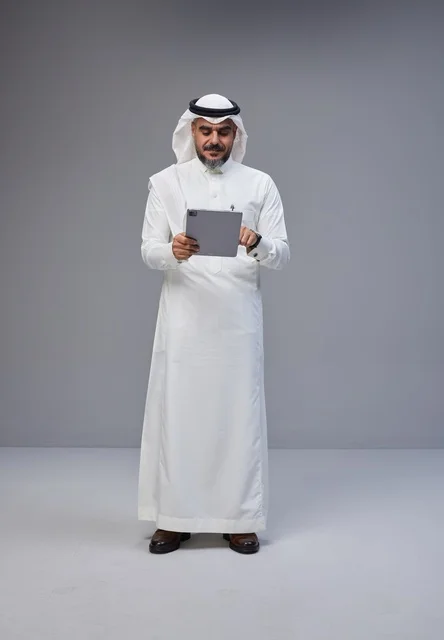 رجل سعودي بالزي التقليدي يستخدم جهازاً لوحياً
