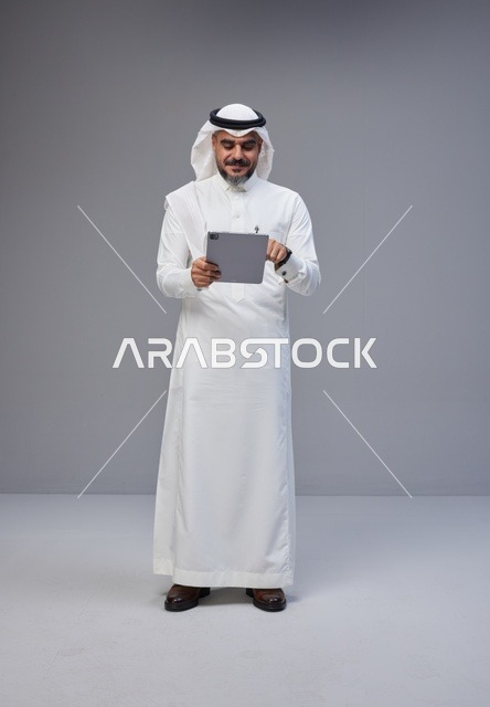 Saudi Man in Traditional Thobe Using Tablet in Studio