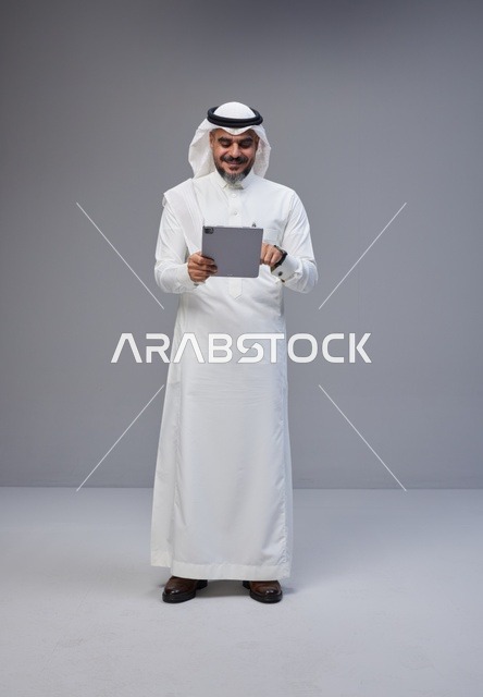 رجل سعودي بالزي التقليدي يستخدم جهازًا لوحيًا