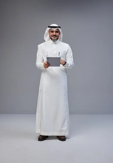 رجل سعودي بالزي التقليدي يستخدم جهازاً لوحياً