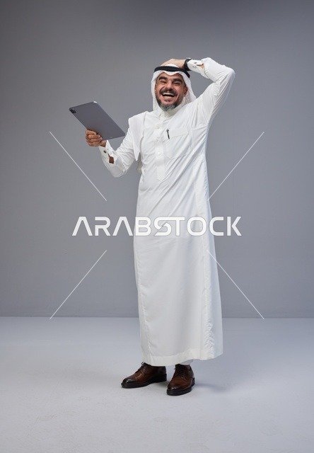 Saudi Man in Traditional Thobe Laughing with Tablet