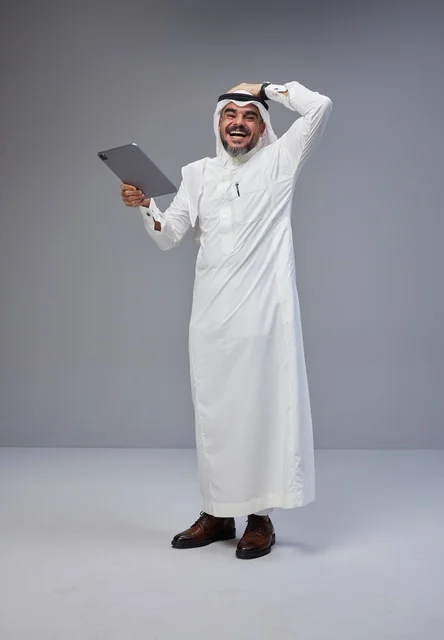 Saudi Man in Traditional Thobe Laughing with Tablet