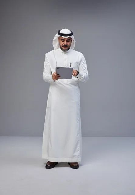 رجل سعودي بالزي التقليدي يستخدم جهازاً لوحياً