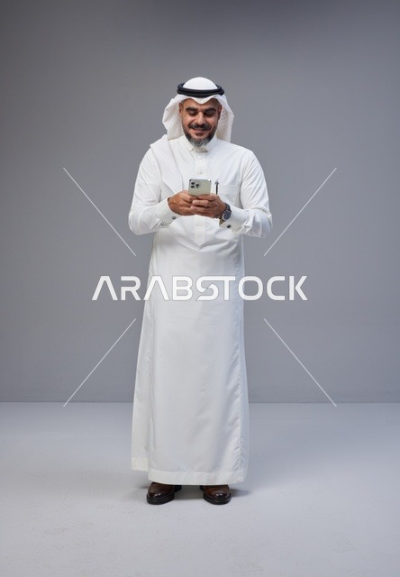 رجل سعودي بالزي التقليدي يستخدم الهاتف الذكي