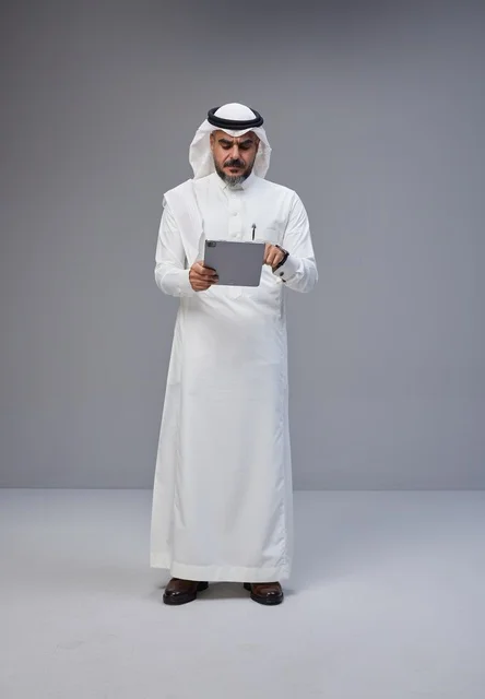 رجل سعودي بالزي التقليدي يستخدم جهازاً لوحياً