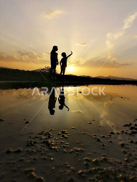 Silhouette of a boy and girl standing in front of a lake during sunset, silhouette, sunset, beauty of nature at sunset, picturesque nature in Saudi Arabia