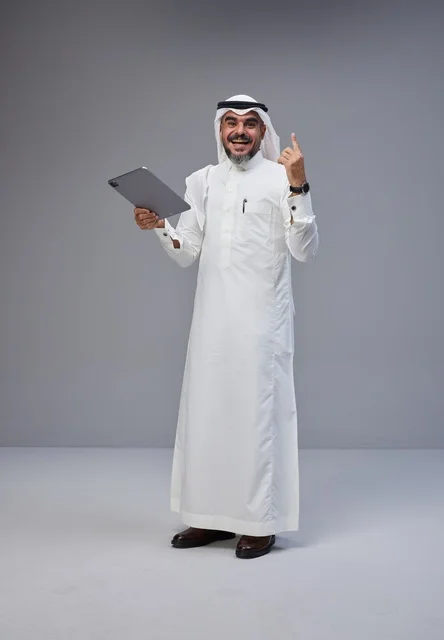 رجل سعودي بالزي التقليدي يستخدم جهازا لوحيا في الاستوديو
