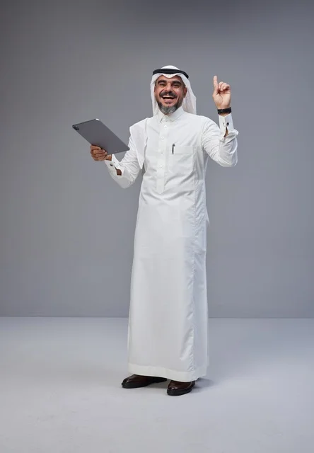 رجل سعودي يحمل جهاز لوحي ويشير للأعلى في الاستوديو