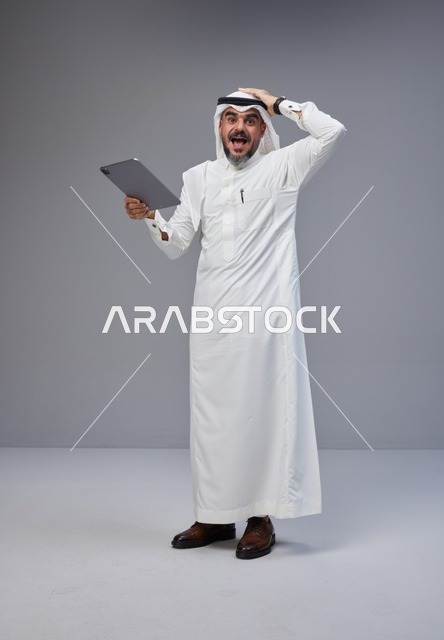 Surprised Saudi Man with Tablet on Grey Background