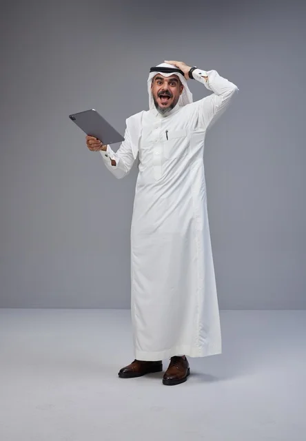 رجل سعودي مندهش يستخدم جهازاً لوحياً بخلفية رمادية
