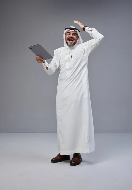 رجل سعودي مع جهاز لوحي يحتفل بالنجاح على خلفية رمادية