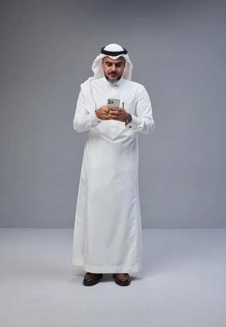 رجل سعودي بالزي التقليدي يستخدم الهاتف الذكي في استوديو