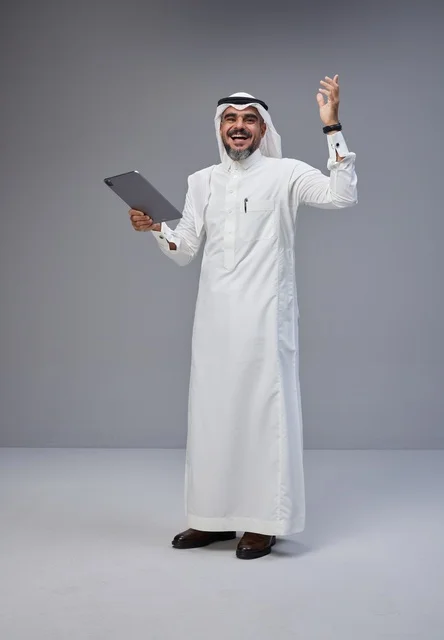 رجل سعودي بالزي التقليدي يستخدم جهازاً لوحياً