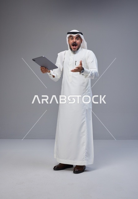 رجل سعودي مندهش يحمل جهاز لوحي بتعبيرات وجه مصدومة