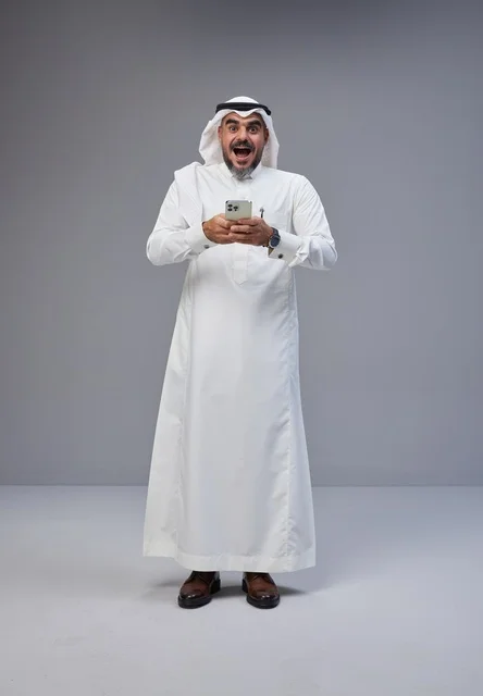رجل سعودي بالزي التقليدي ممسكاً بهاتف ذكي بتعبير مندهش