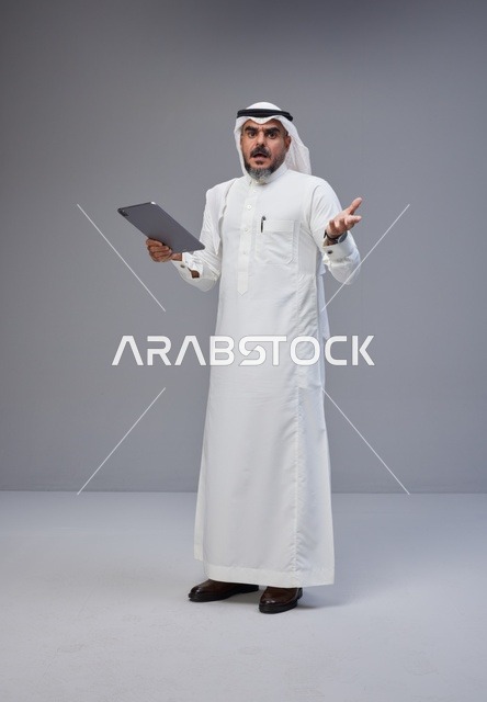 رجل سعودي مع جهاز لوحي بتعبير وجه مصدوم في الاستوديو