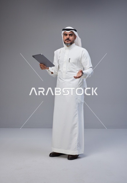 رجل سعودي بالزي التقليدي يحمل جهازاً لوحيًا