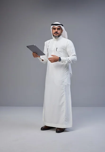 رجل سعودي بالزي التقليدي يستخدم جهازًا لوحيًا