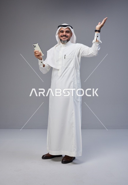 رجل سعودي بالزي التقليدي يستخدم الهاتف الذكي في استوديو