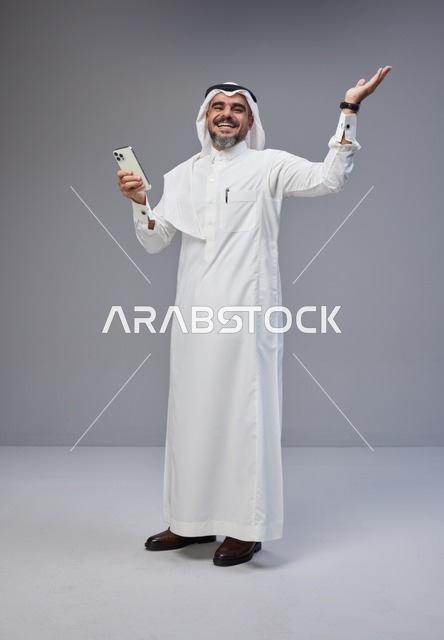 رجل سعودي يبتسم ويستخدم الهاتف الذكي في الاستوديو
