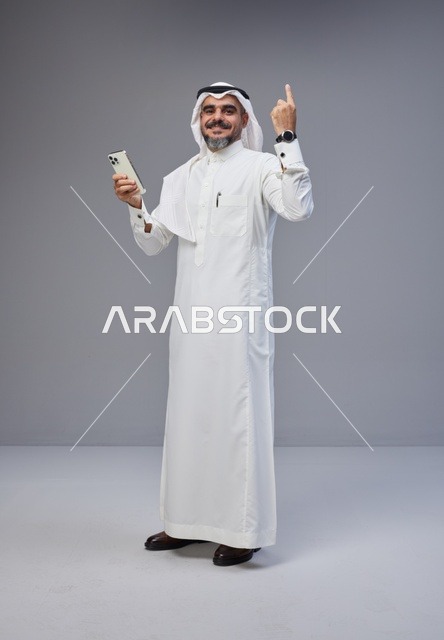 Saudi Man in Thobe with Smartphone Pointing Up