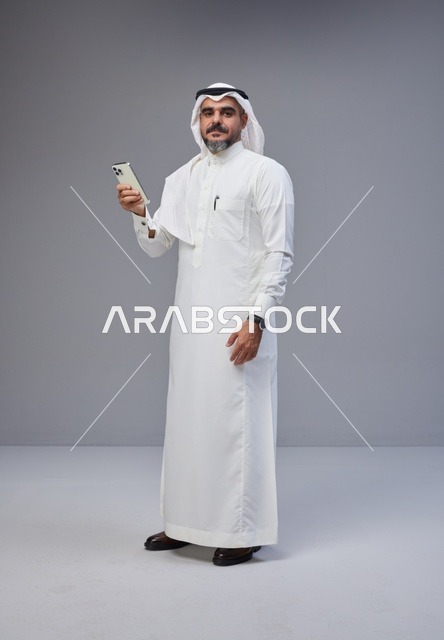 رجل سعودي بالزي التقليدي يستخدم الهاتف الذكي