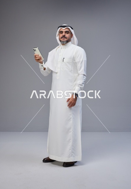رجل سعودي بالزي التقليدي يستخدم الهاتف الذكي
