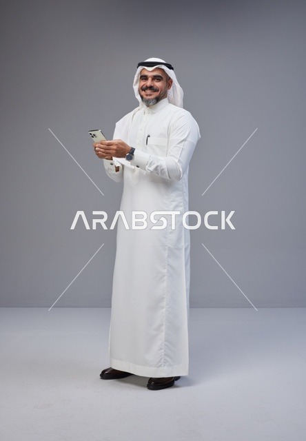 رجل سعودي بالزي التقليدي يستخدم الهاتف الذكي