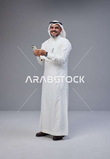 رجل سعودي بالزي التقليدي يستخدم الهاتف الذكي