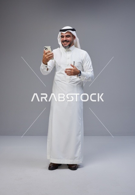 رجل سعودي بالزي التقليدي يستخدم هاتف ذكي