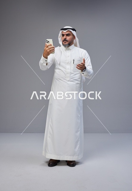 رجل سعودي بالزي التقليدي يستخدم الهاتف الذكي