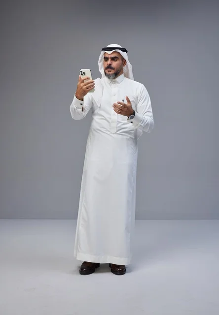 رجل سعودي بالزي التقليدي يستخدم الهاتف في الاستوديو