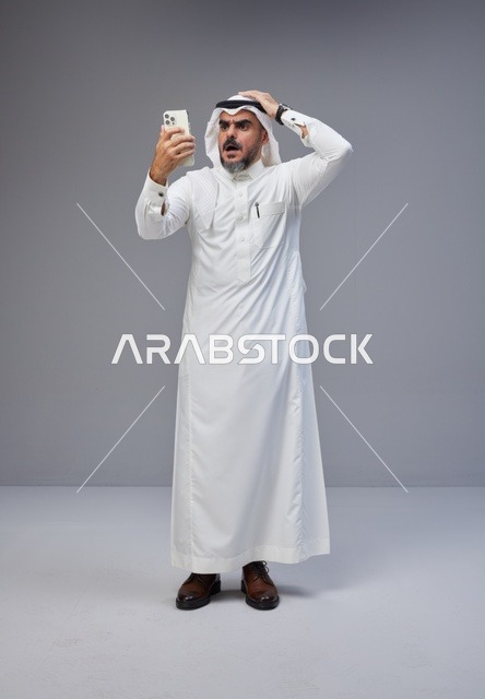 رجل سعودي بالثوب التقليدي مصدوم من الهاتف الذكي