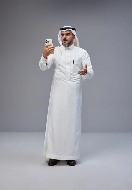 رجل سعودي بالزي التقليدي يستخدم الهاتف الذكي