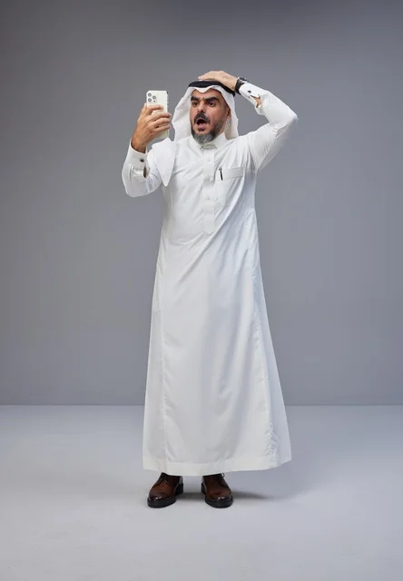 رجل سعودي بالزي التقليدي يشعر بالصدمة عند استخدام الهاتف