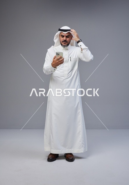 رجل سعودي بالزي التقليدي يستخدم الهاتف الذكي
