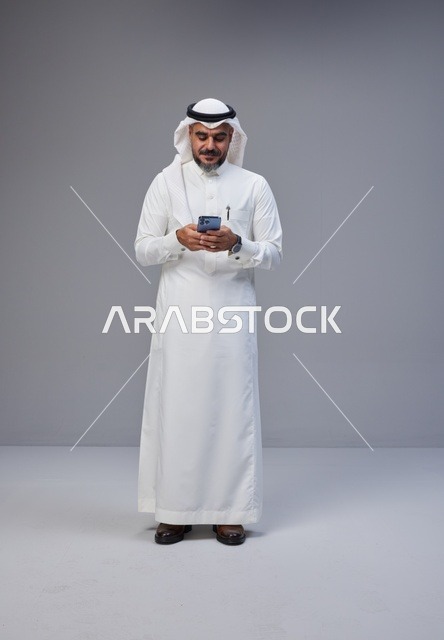 رجل سعودي بالزي التقليدي يستخدم الهاتف الذكي