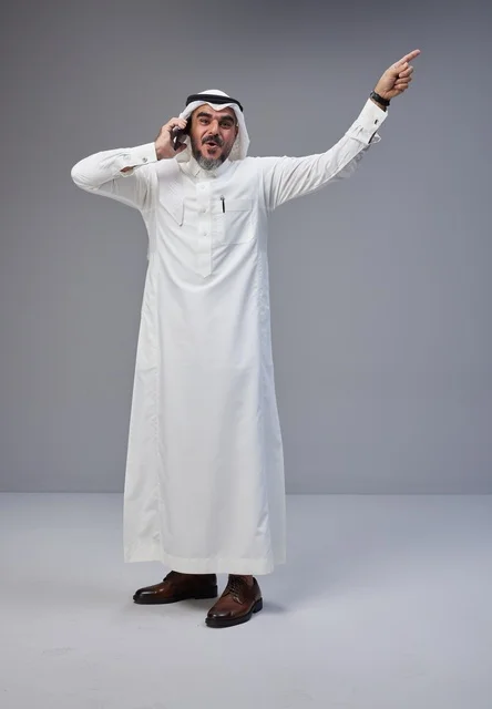 رجل سعودي بالزي التقليدي يتحدث عبر الجوال ويشير للأعلى
