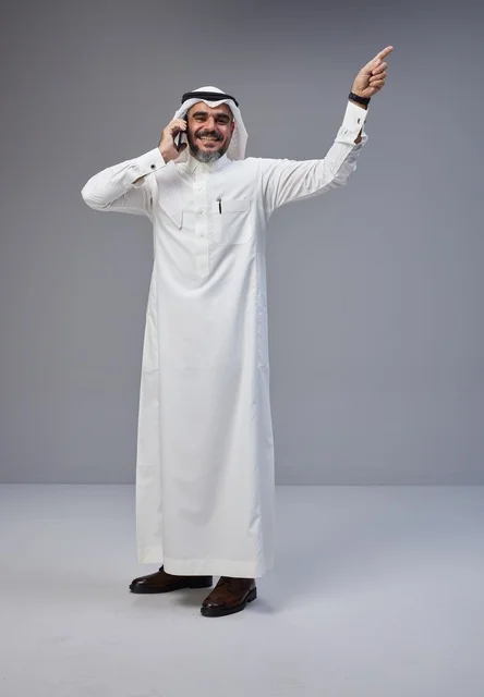 رجل سعودي بالزي التقليدي يتحدث بالهاتف ويشير للأعلى
