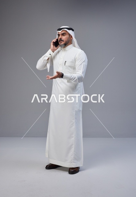 رجل سعودي بالزي التقليدي يتحدث عبر الهاتف مع إيماءة تعبيرية