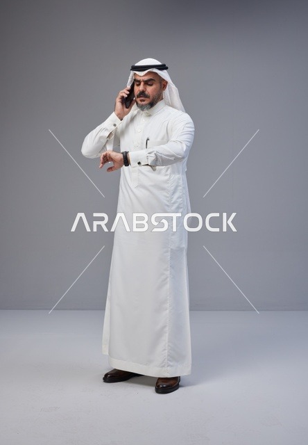 رجل سعودي بالزي التقليدي يتحدث بالهاتف وينظر للساعة
