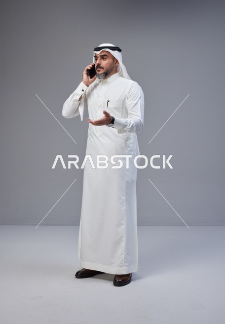 رجل سعودي يتحدث عبر الهاتف الجوال في استوديو بخلفية رمادية