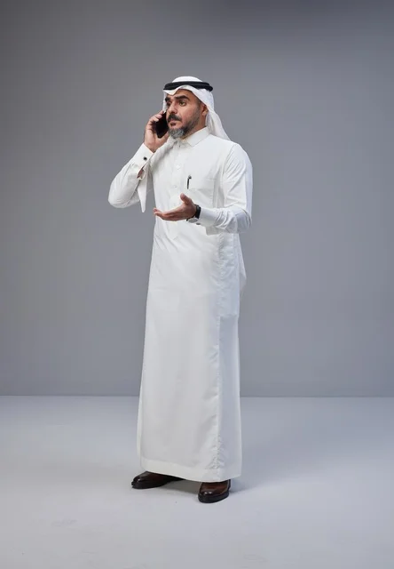 رجل سعودي يتحدث عبر الهاتف الجوال في استوديو بخلفية رمادية