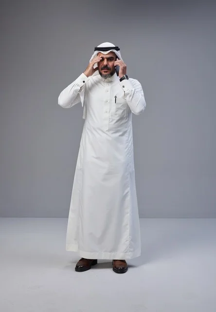 رجل سعودي بالزي التقليدي يتحدث بالهاتف بتعبير قلق