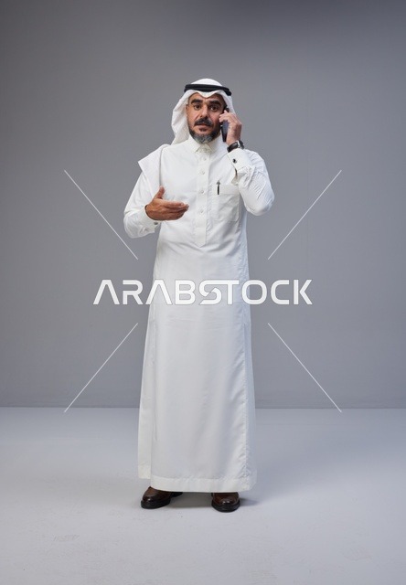 رجل سعودي بالثوب يتحدث بالهاتف مع إيماءة تعبيرية