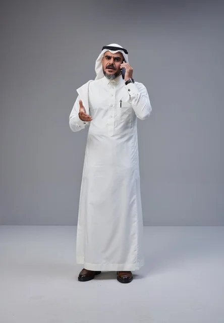رجل سعودي بالزي التقليدي يتحدث عبر الهاتف بإيماءة يد