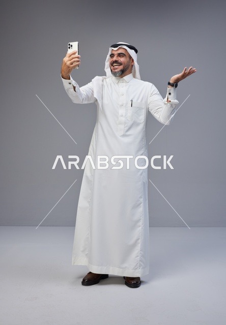 Saudi man in traditional attire taking a selfie with smartphone